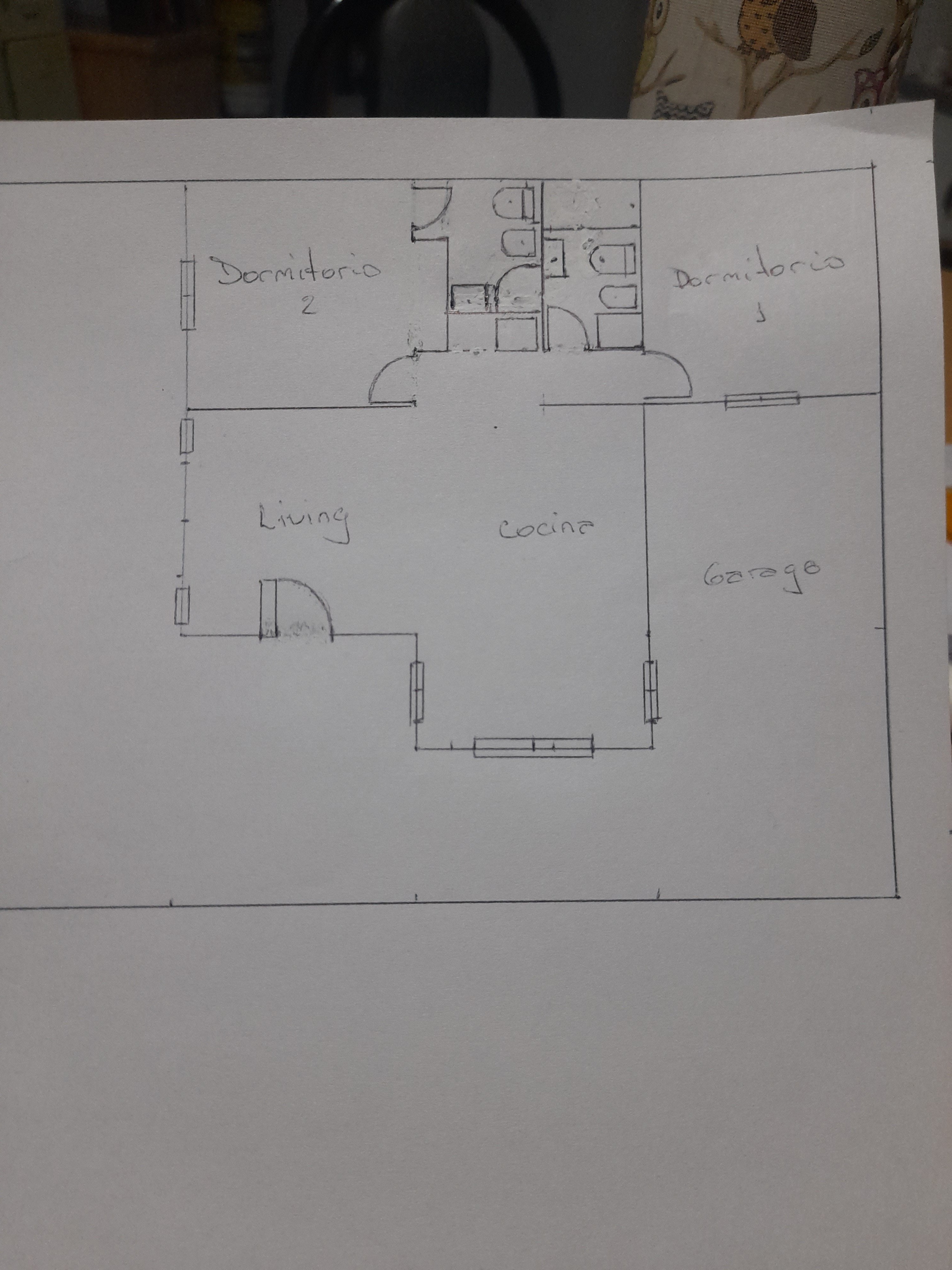 Photographed hand-drawn house plan with two bedrooms, bathrooms, a living and kitchen area, and a garage